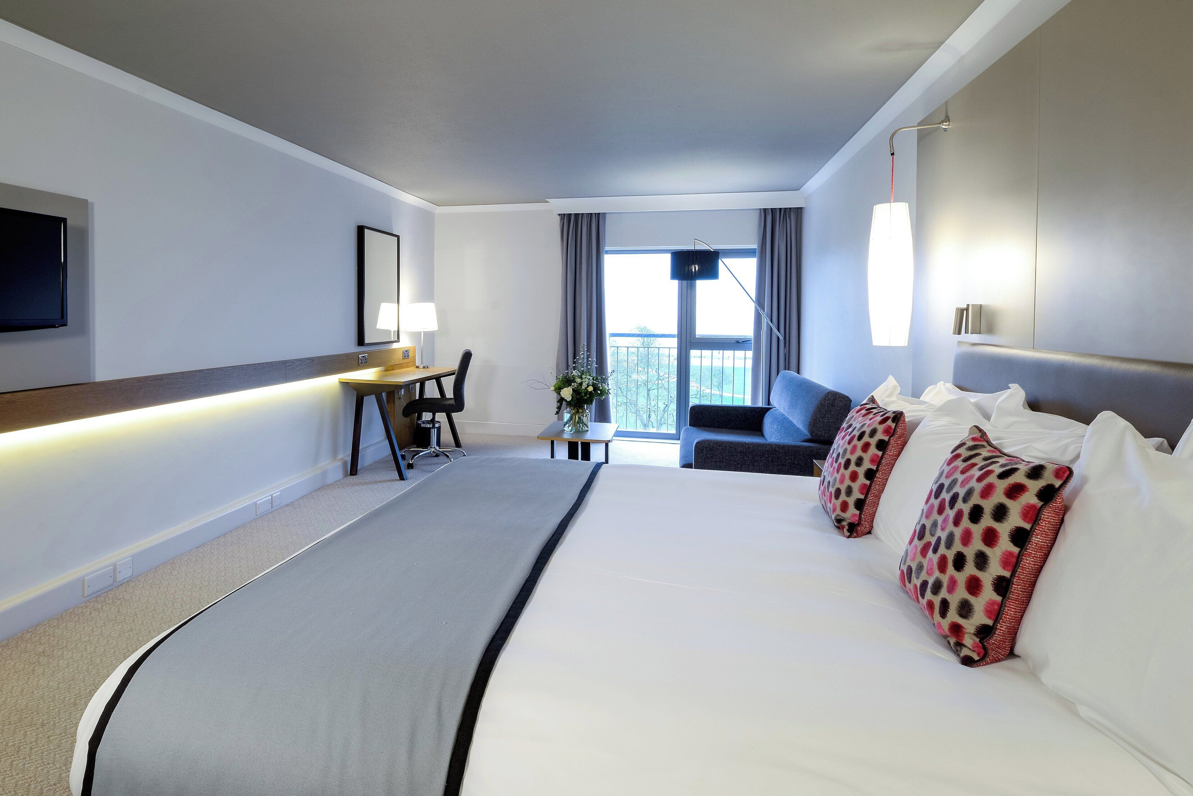 A hotel room with a bed, a desk, a chair, a TV, and a window with curtains.