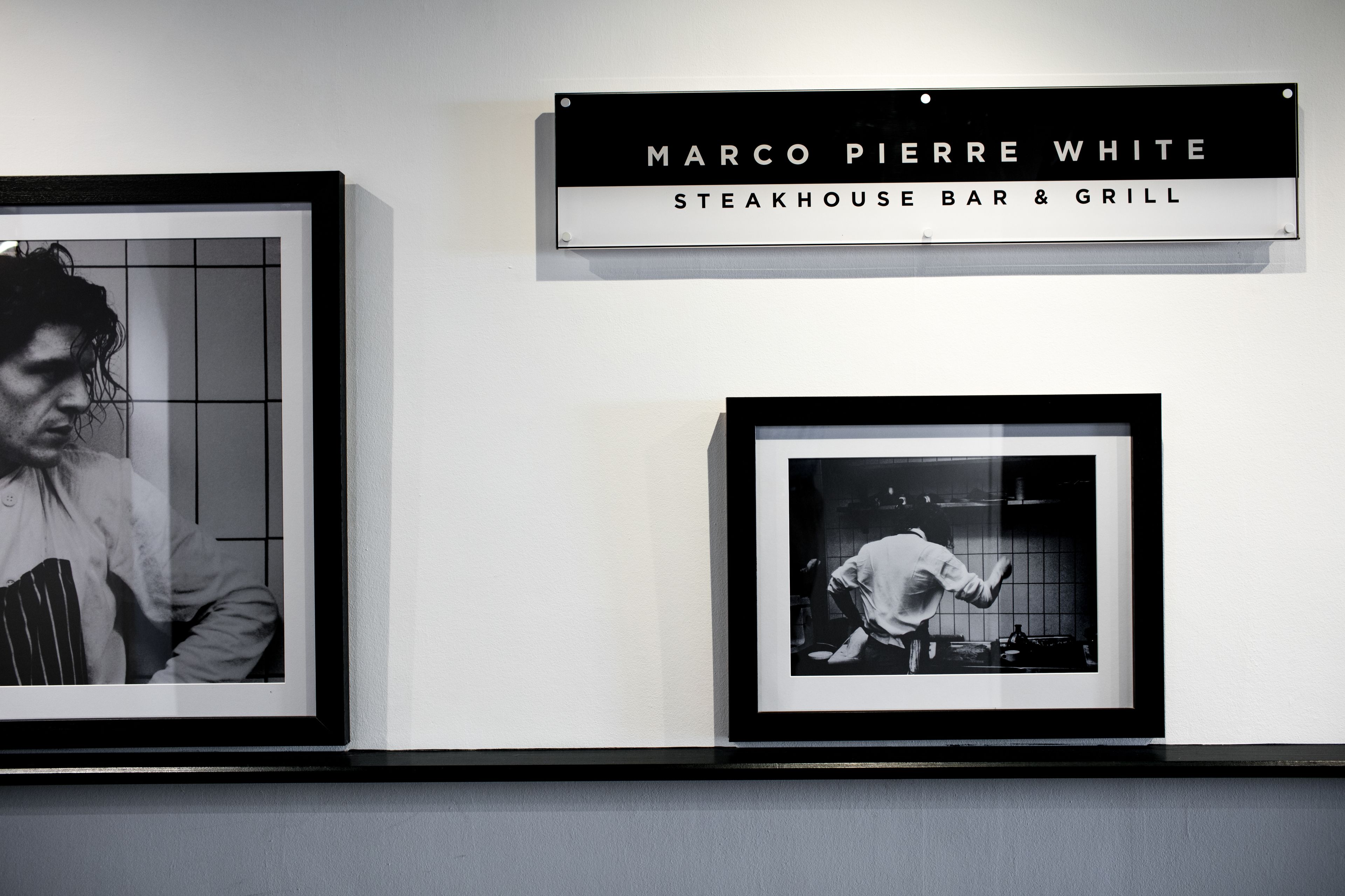 A wall with two framed black and white photographs and a sign above them.