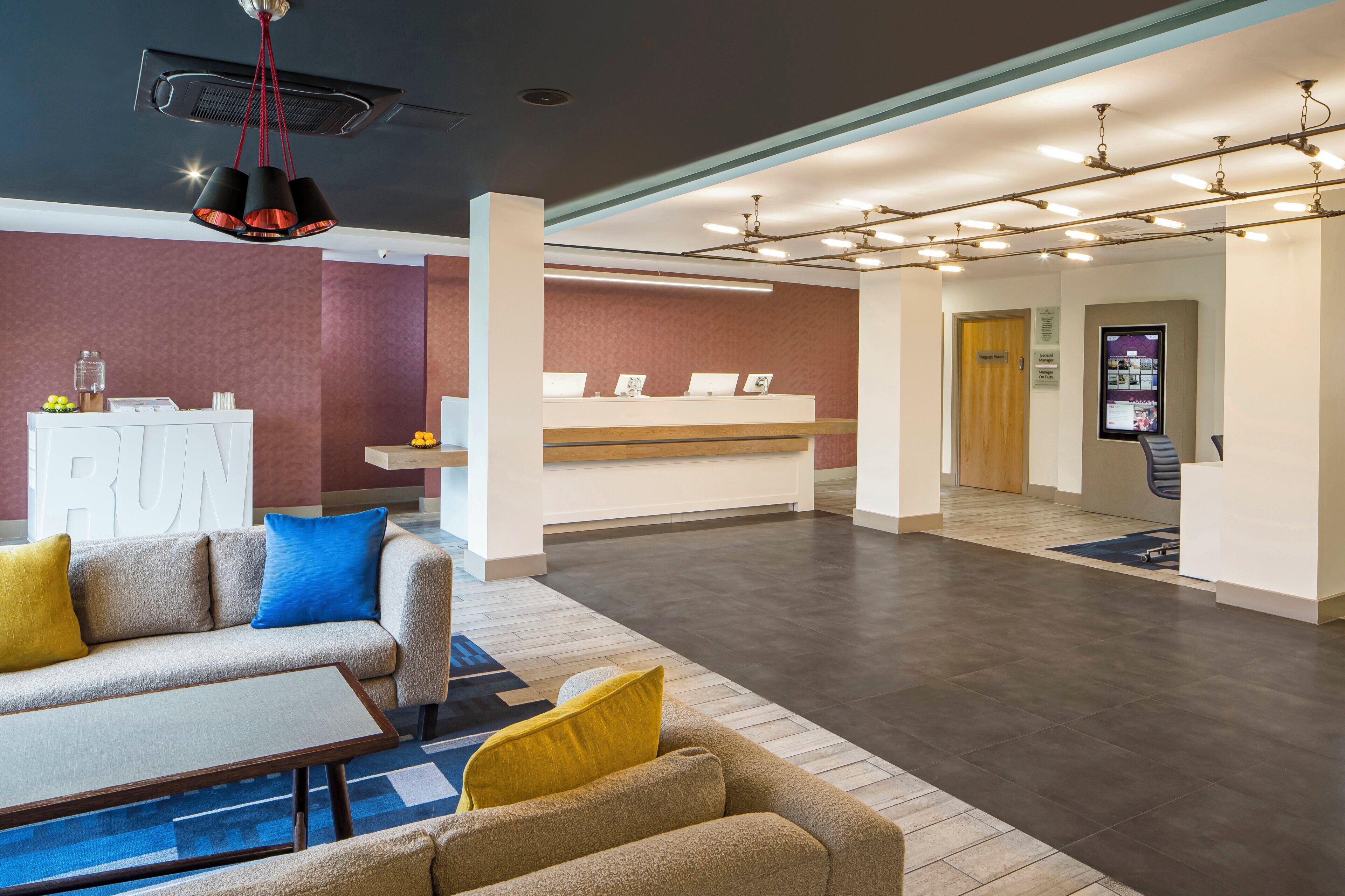 Eine moderne Hotelhalle mit Rezeption, Sitzgelegenheiten und einem digitalen Informationsbildschirm.