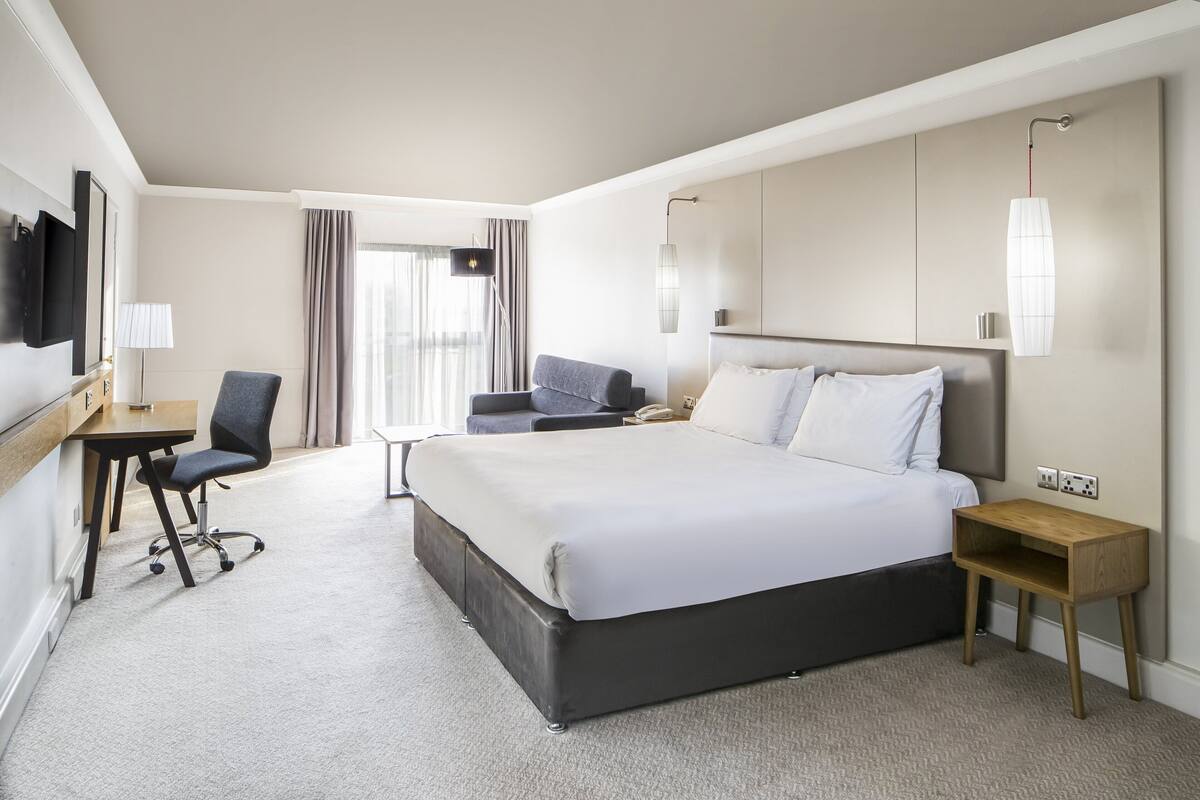 A modern hotel room with a large bed, a desk, a chair, and a TV mounted on the wall.