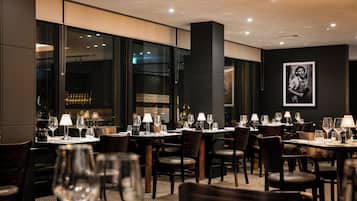 Een restaurantinterieur met gedekte tafels, stoelen en een barruimte zichtbaar door het raam.
