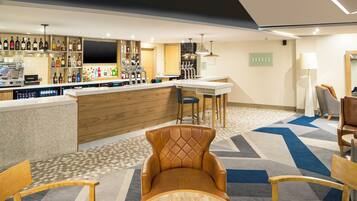 Un espace bar avec un comptoir, des étagères remplies de bouteilles d’alcool et un téléviseur. On peut voir des chaises et une table au premier plan.