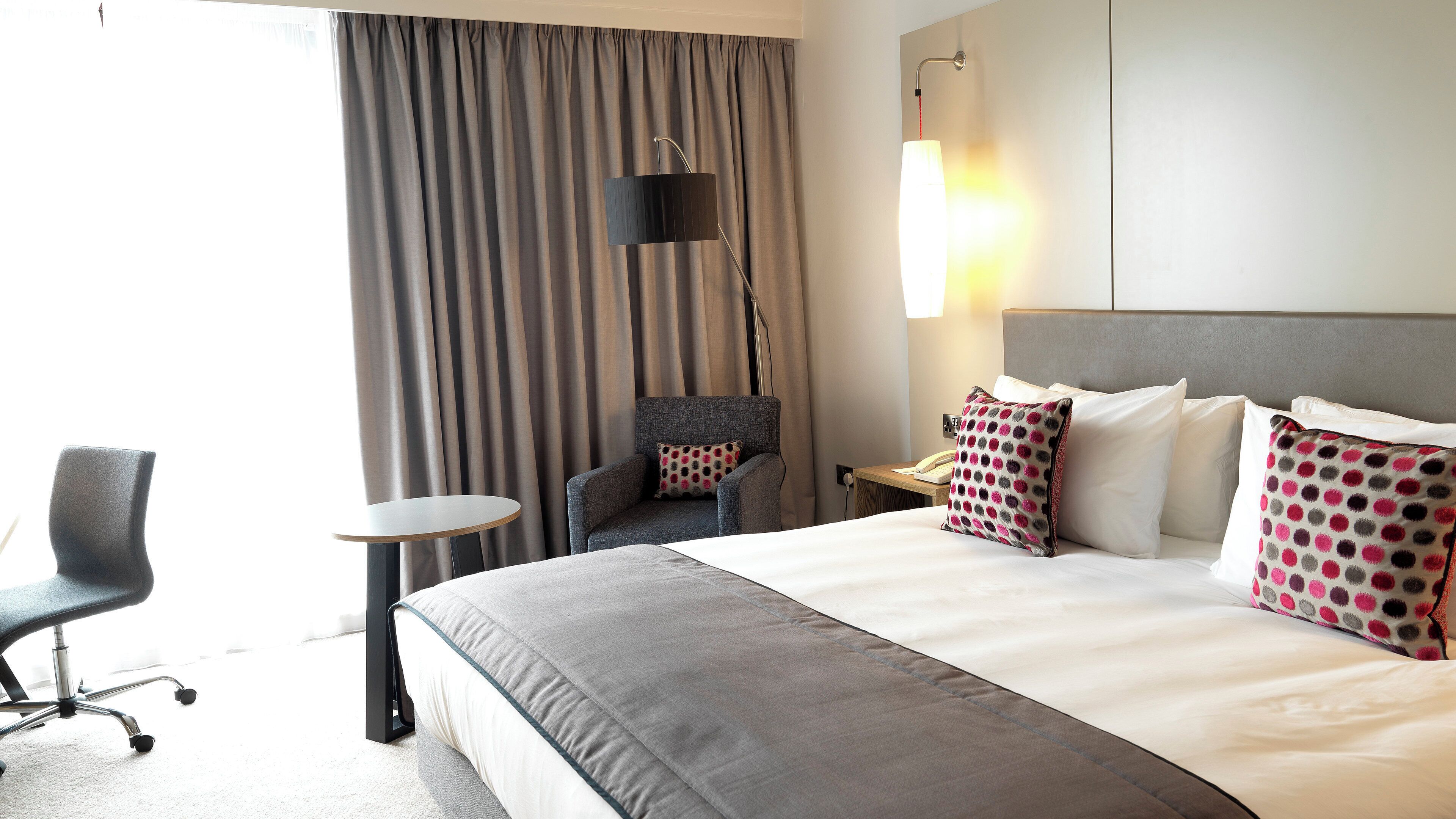 A hotel room with a large bed, a desk, a chair, and a window with curtains.