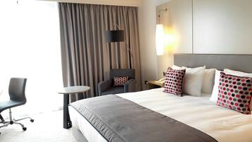 A hotel room with a large bed, a desk, a chair, and a window with curtains.