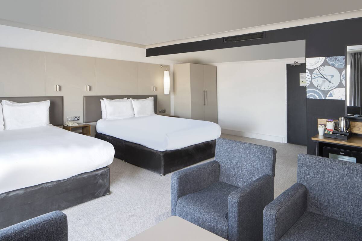 A hotel room with two beds, a desk, and a seating area.