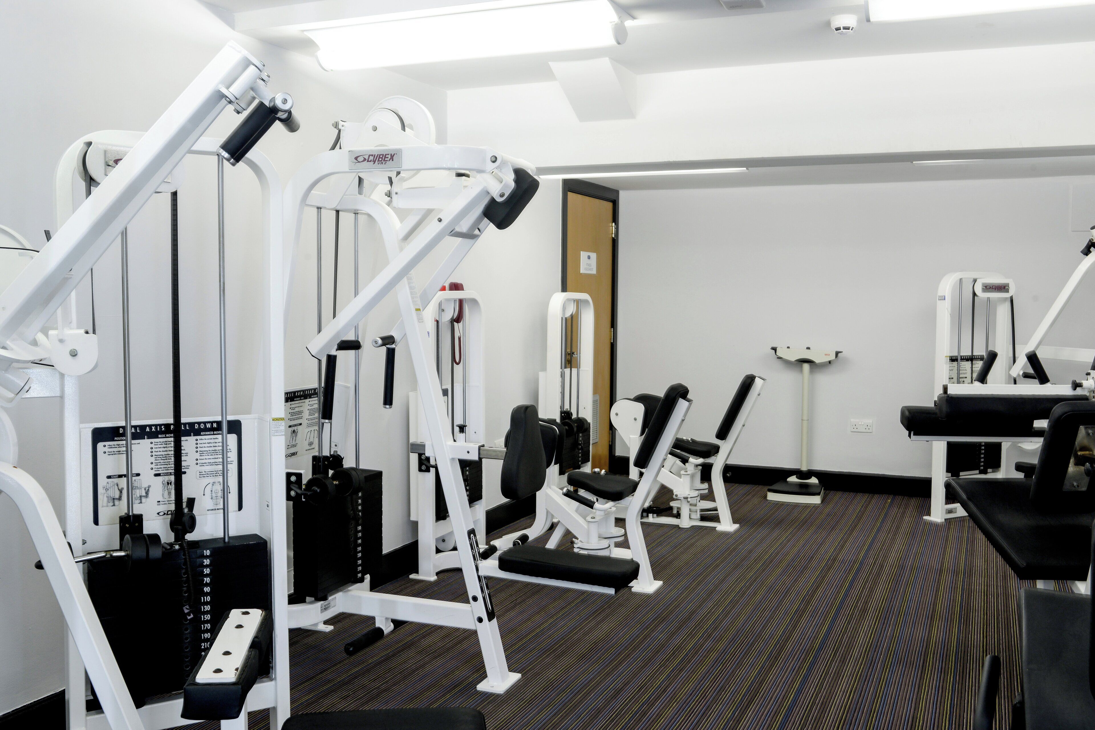 A gym with various exercise machines, a door, and a carpeted floor.