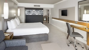 A hotel room with a large bed, a desk with a chair, a flat-screen TV, and a large mirror.