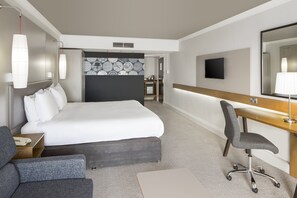 A hotel room with a large bed, a desk with a chair, a flat-screen TV, and a large mirror.
