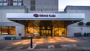 The entrance of Crowne Plaza hotel with a modern facade, a covered entrance, and a visible seating area outside.