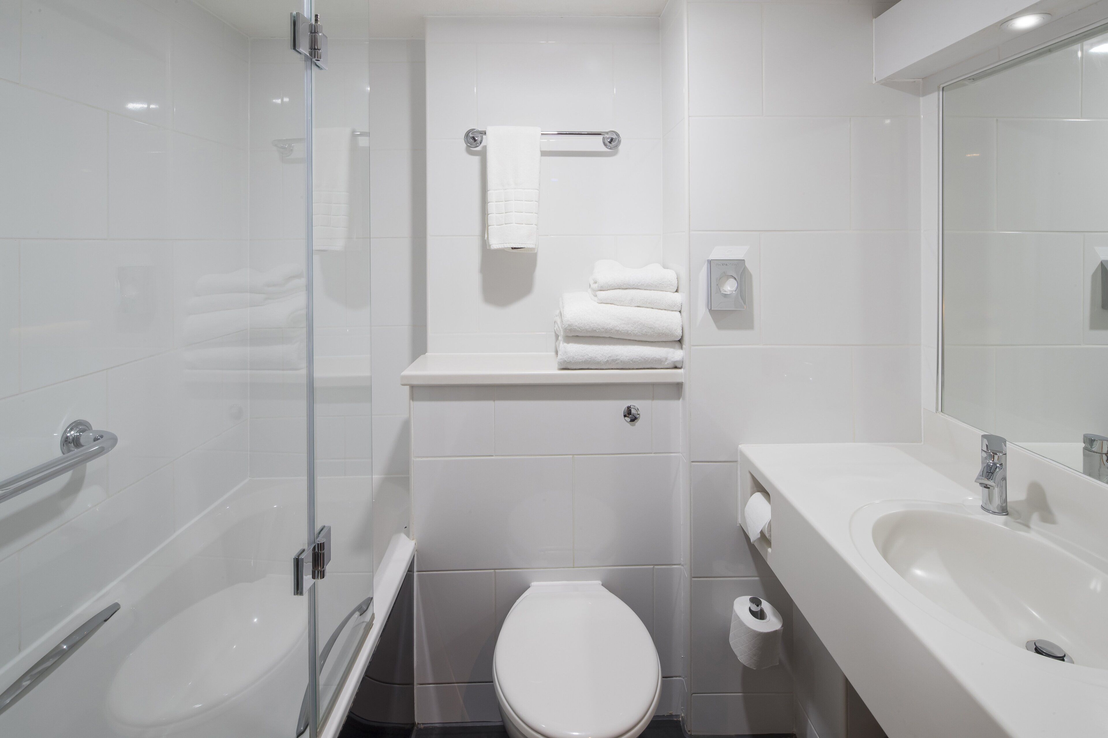A modern bathroom with a glass shower enclosure, a white toilet, a sink with a mirror, and neatly stacked towels.