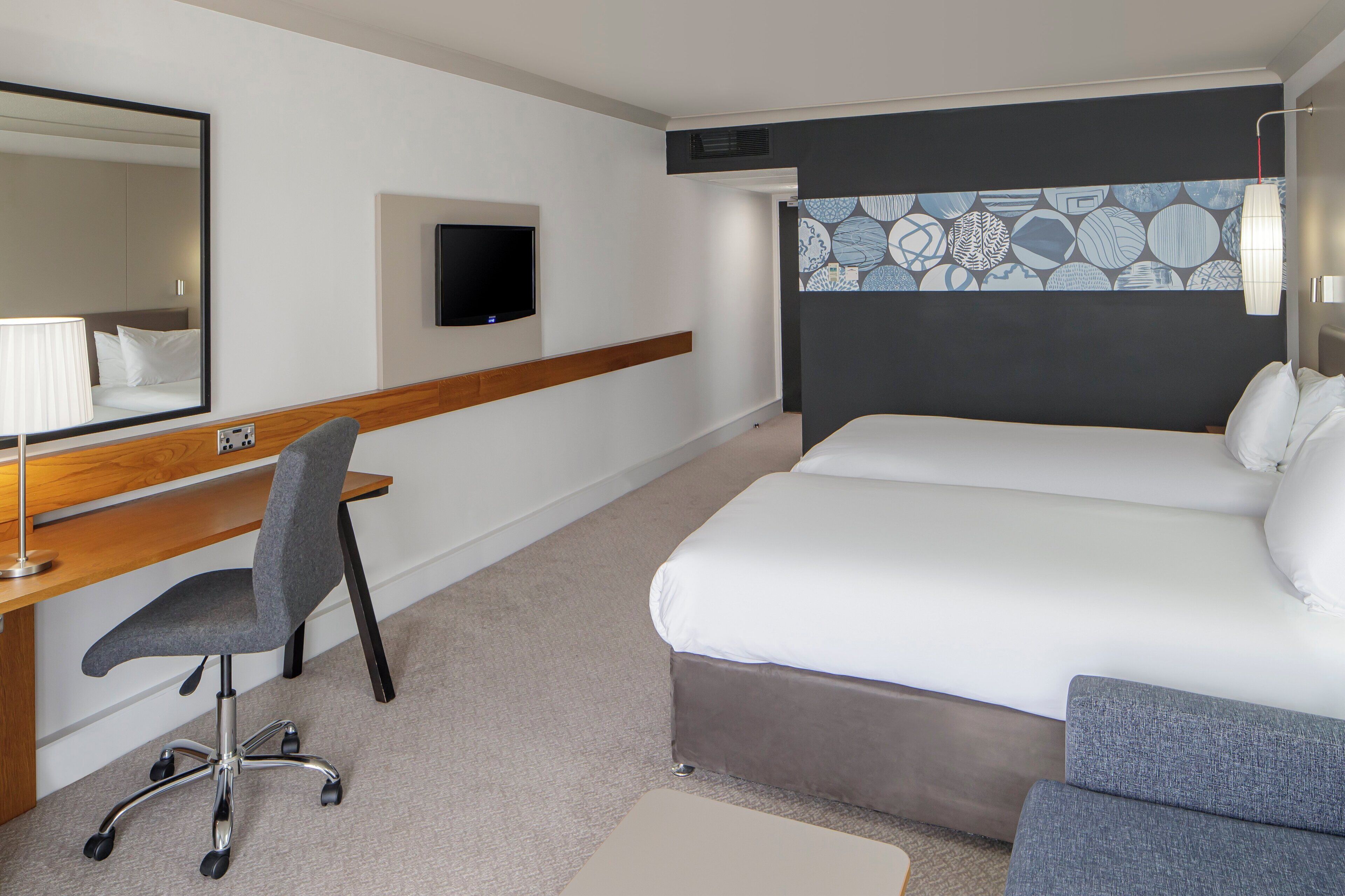Een hotelkamer met een bed, een bureau, een stoel, een televisie en een behang met een patroon.