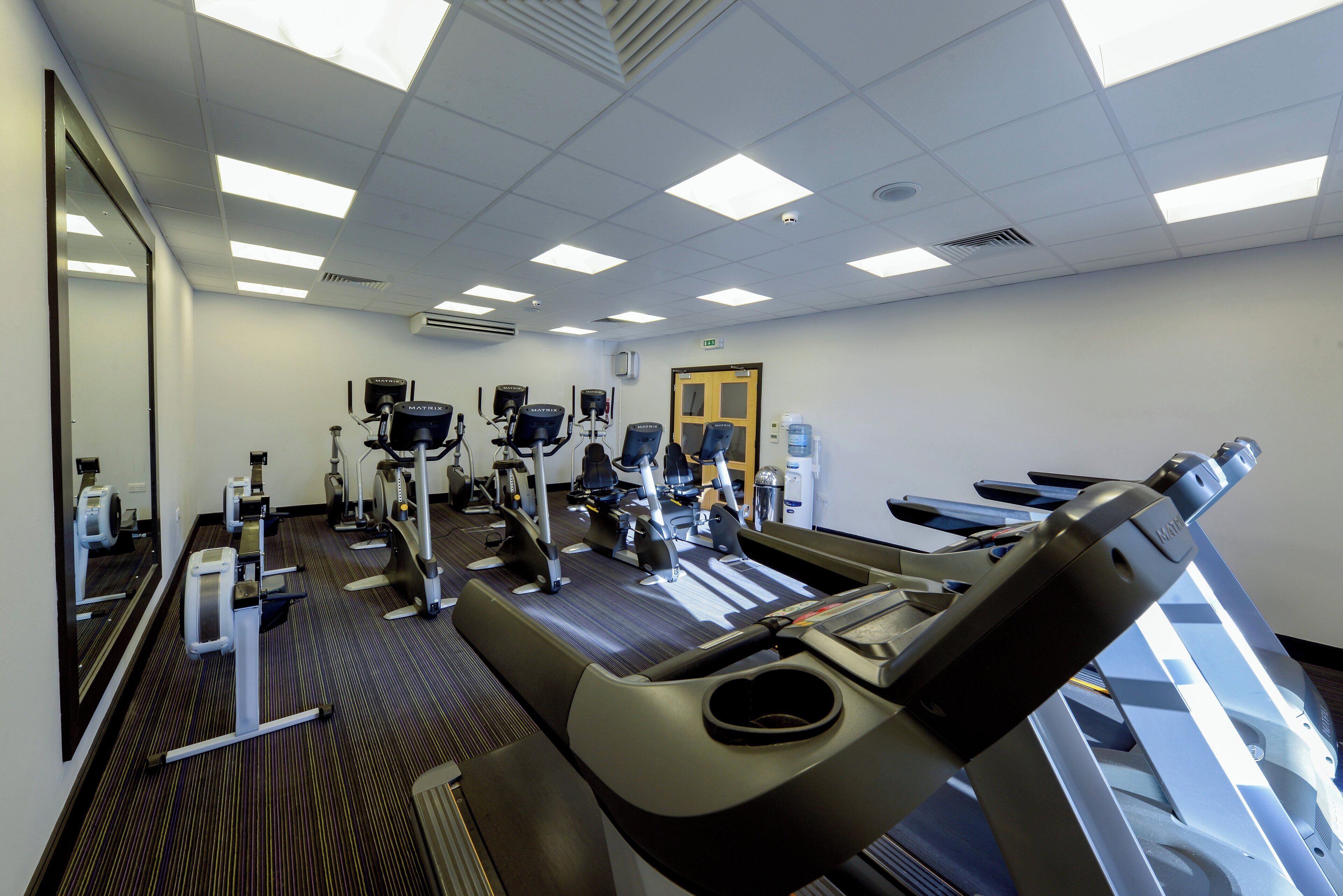 A gym with various exercise equipment, a mirrored wall, and a patterned carpet.