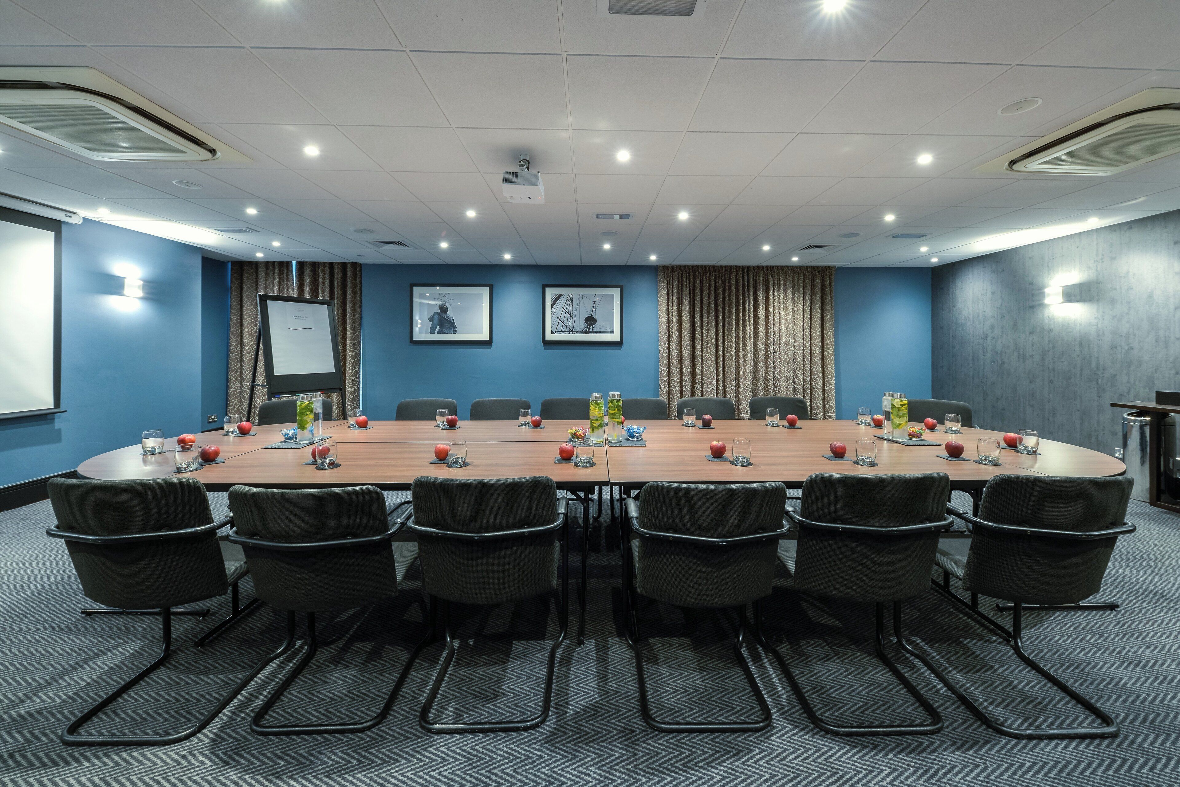 Ett konferensrum med ett långt bord, stolar och inramade tavlor på väggarna.