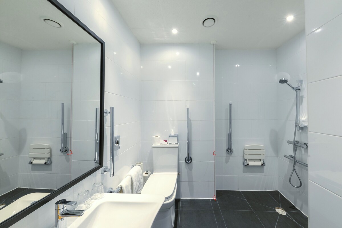 A modern bathroom with a large mirror, a dual sink vanity, a toilet, and a shower area.