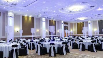 Un salón de banquetes con mesas redondas, sillas negras y blancas, y candelabros de cristal decorativos.