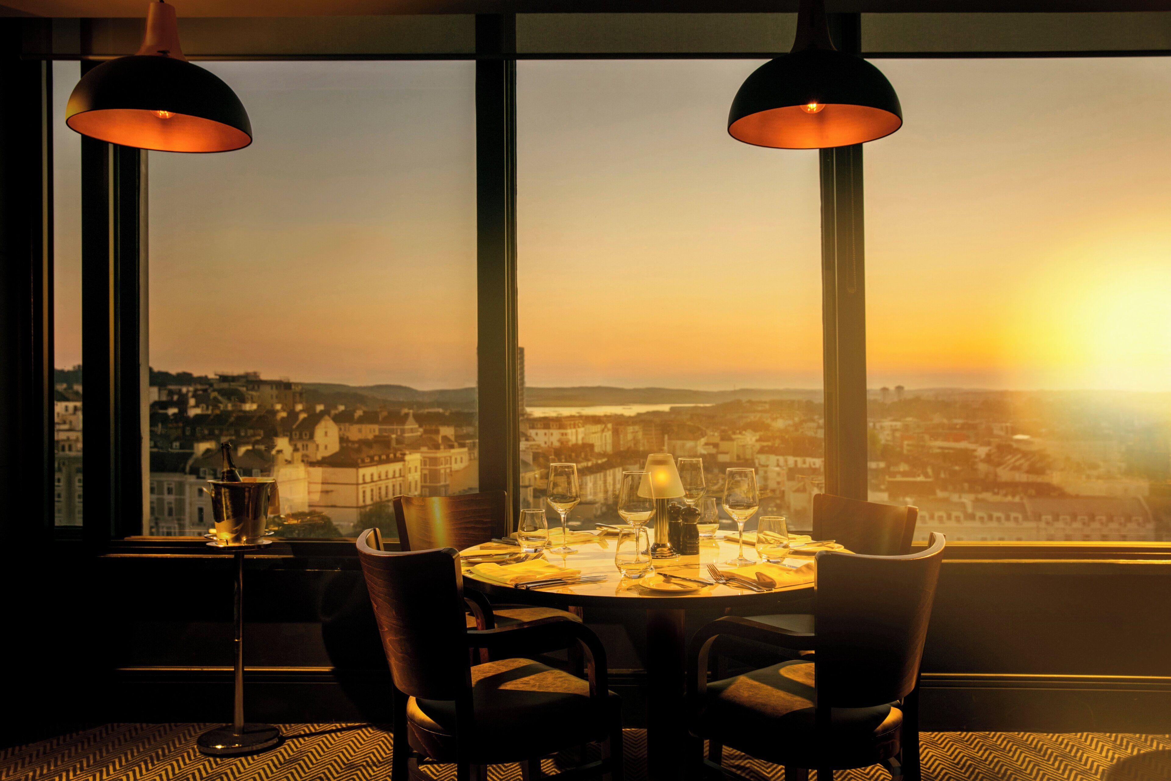 Una mesa de comedor con sillas y vistas a un paisaje urbano al atardecer.