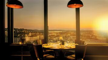 A dining table with chairs and a view of a cityscape at sunset.
