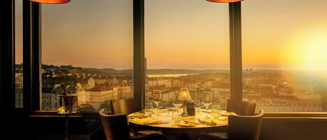 Una mesa de comedor con sillas y vistas a un paisaje urbano al atardecer.