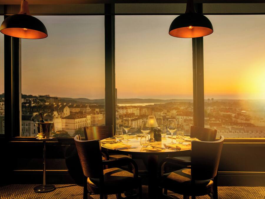 Una mesa de comedor con sillas y vistas a un paisaje urbano al atardecer.
