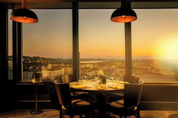 Una mesa de comedor con sillas y vistas a un paisaje urbano al atardecer.