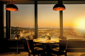 A dining table with chairs and a view of a cityscape at sunset. - Crowne Plaza Plymouth by IHG (Plymouth)