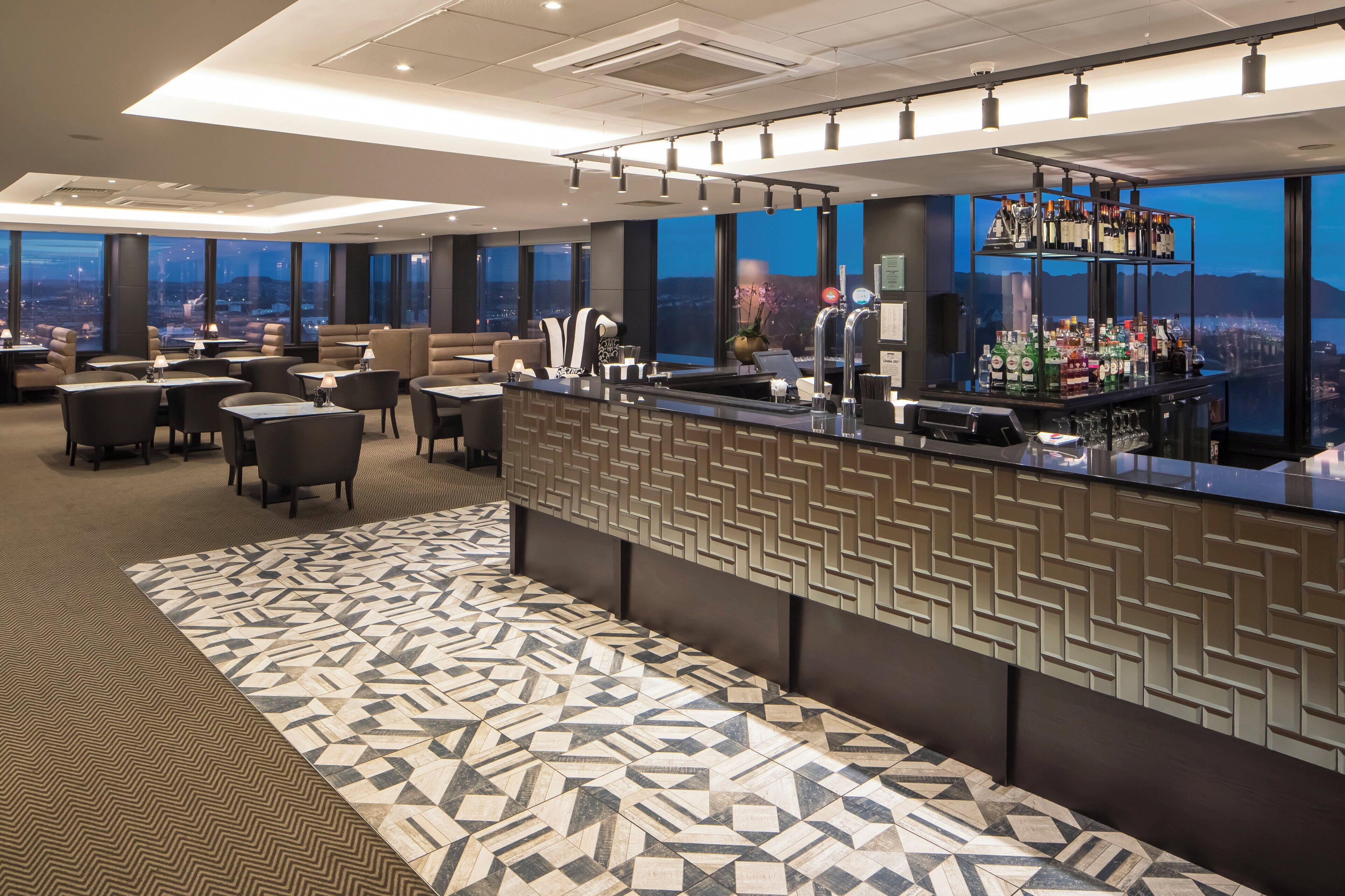 A modern bar area with a patterned floor, seating, and a city view.