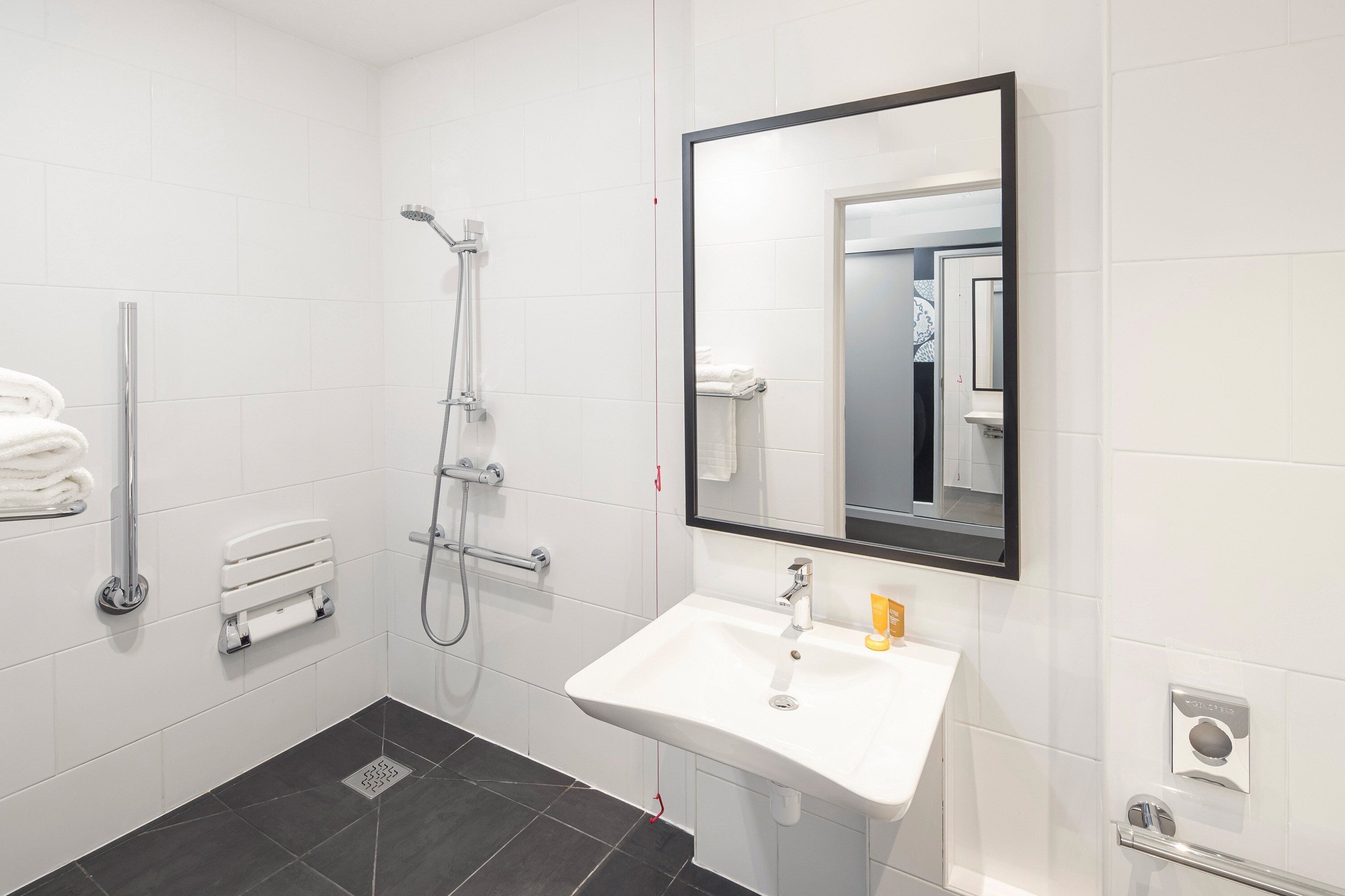 Een moderne badkamer met een witte wastafel, een grote spiegel en een douche met een handdouche.