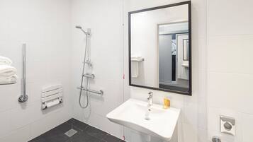 A modern bathroom with a white sink, a large mirror, and a shower with a handheld showerhead.
