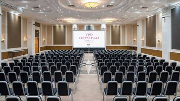 Un salón de conferencias con filas de sillas que dan a una pantalla de proyección que muestra 'CROWNE PLAZA AN IHG HOTEL PLYMOUTH'.