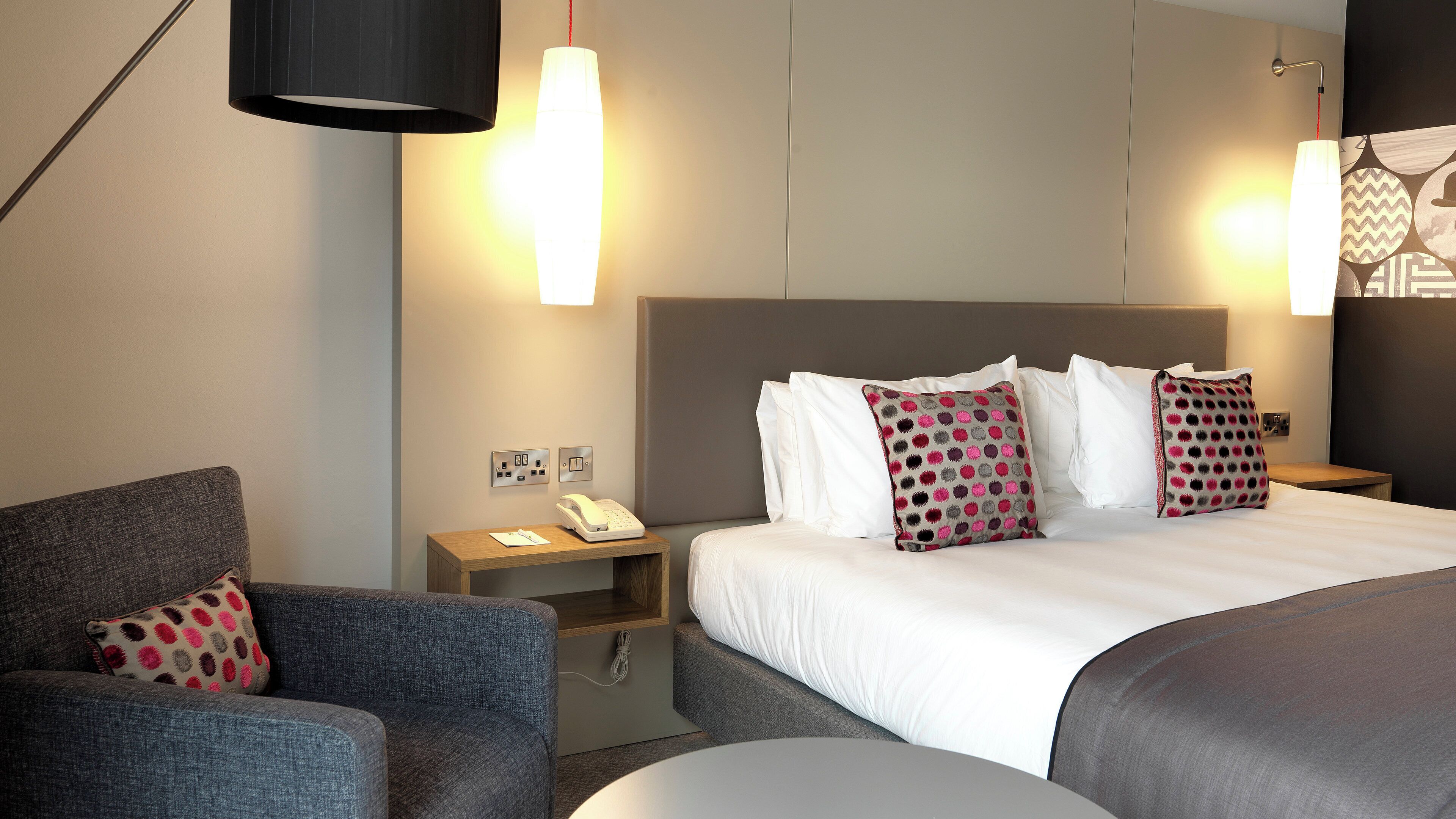 Ein Hotelzimmer mit Bett, einem Sessel, einem Nachttisch mit Telefon und einer Wandleuchte.