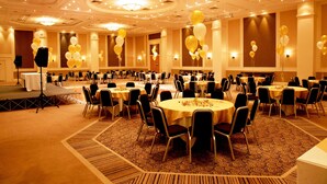 A banquet hall with round tables, chairs, and a stage.