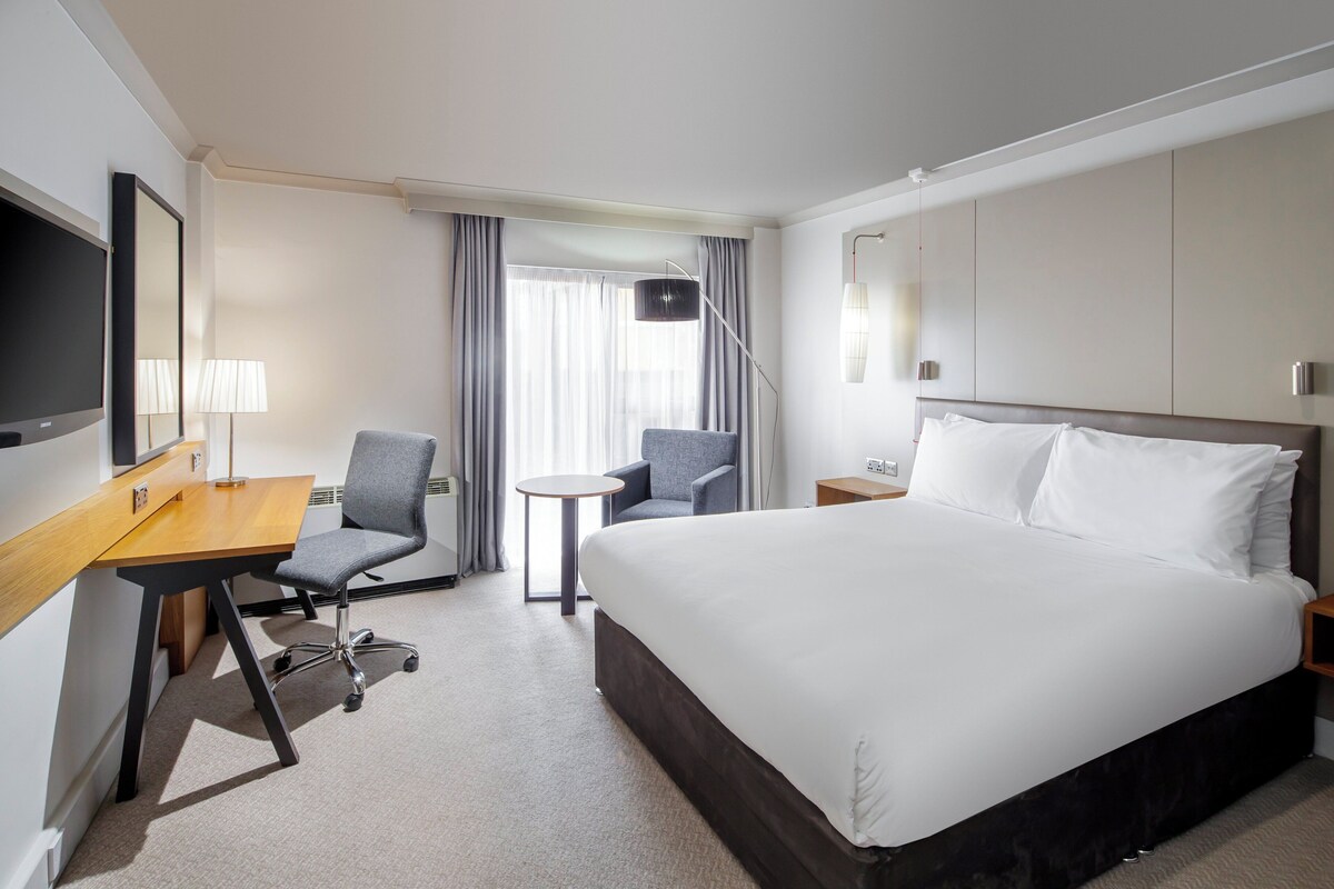 A hotel room with a bed, desk, chair, and a TV.