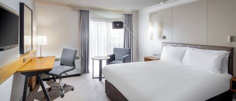A hotel room with a bed, desk, chair, and a TV.