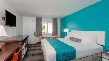 A hotel room with a bed, a desk, a chair, a TV, and a window with curtains.