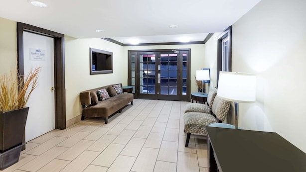 Un vestíbulo de hotel con un mostrador de recepción, un sofá, una silla, una lámpara y una puerta con un letrero.