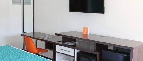 Une chambre d’hôtel équipée d’un lit, d’un bureau, d’un fauteuil orange, d’un téléviseur à écran plat et d’un four à micro-ondes intégré.