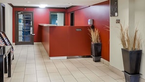 Un área de recepción con un mostrador rojo, puerta de cristal de entrada y suelo de baldosas.
