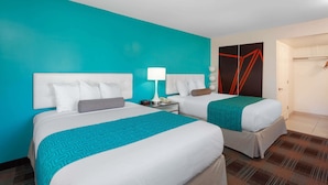 Habitación de hotel con dos camas, una pared de acento color aguamarina, una puerta moderna y un mostrador de recepción.