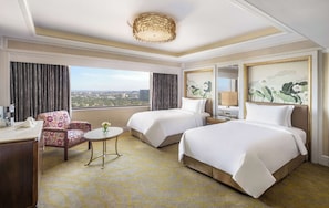 Habitación de hotel con dos camas, un escritorio, una silla, una mesita y vistas a la ciudad.