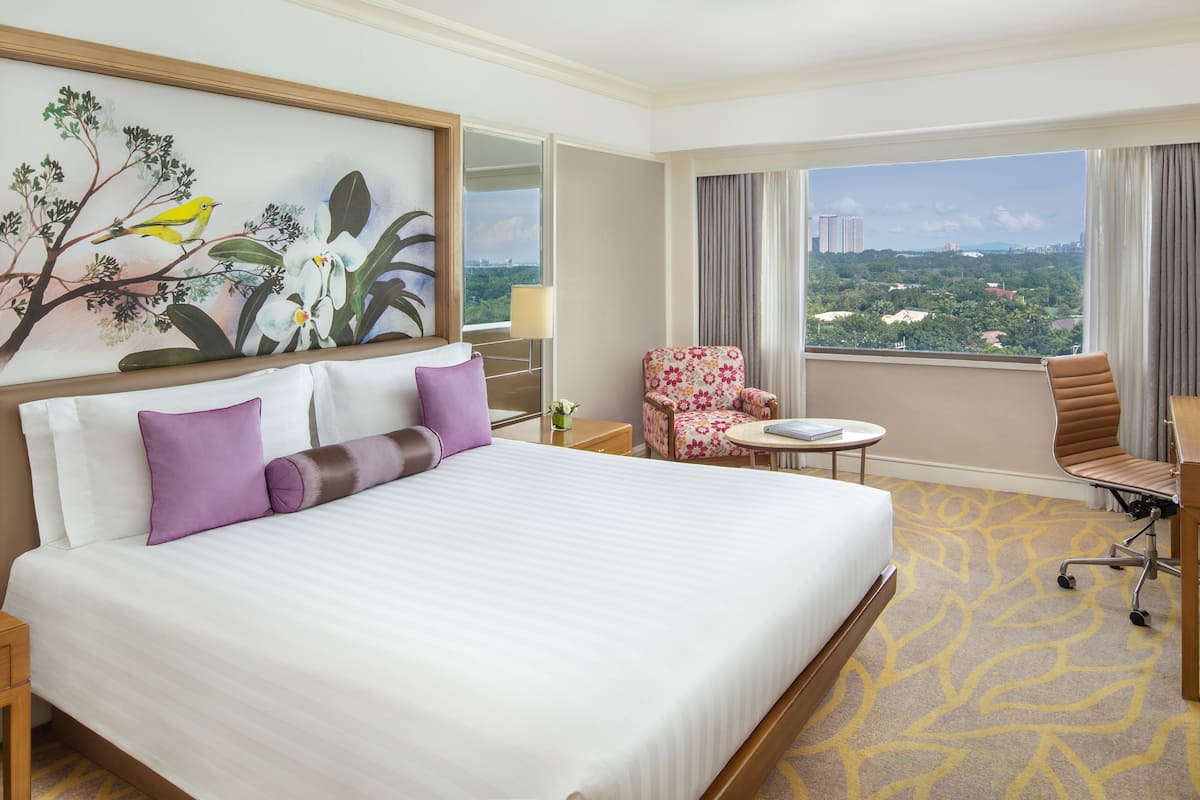 Habitación de hotel con una cama grande, una silla, una mesita y vistas a la ciudad.