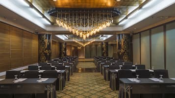 A conference room with rows of tables, a patterned carpet, and a chandelier.