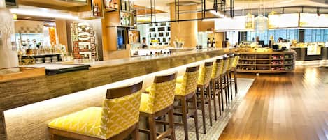 A modern bar area with a long counter, multiple stools, and a variety of bottles and glasses on shelves.