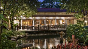 A traditional-style building with a covered outdoor dining area, a small pond, and lush greenery. - Dusit Thani Manila (Makati)