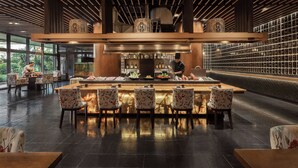 A restaurant with a bar area, wooden ceiling, and a chef preparing food. - Dusit Thani Manila (Makati)