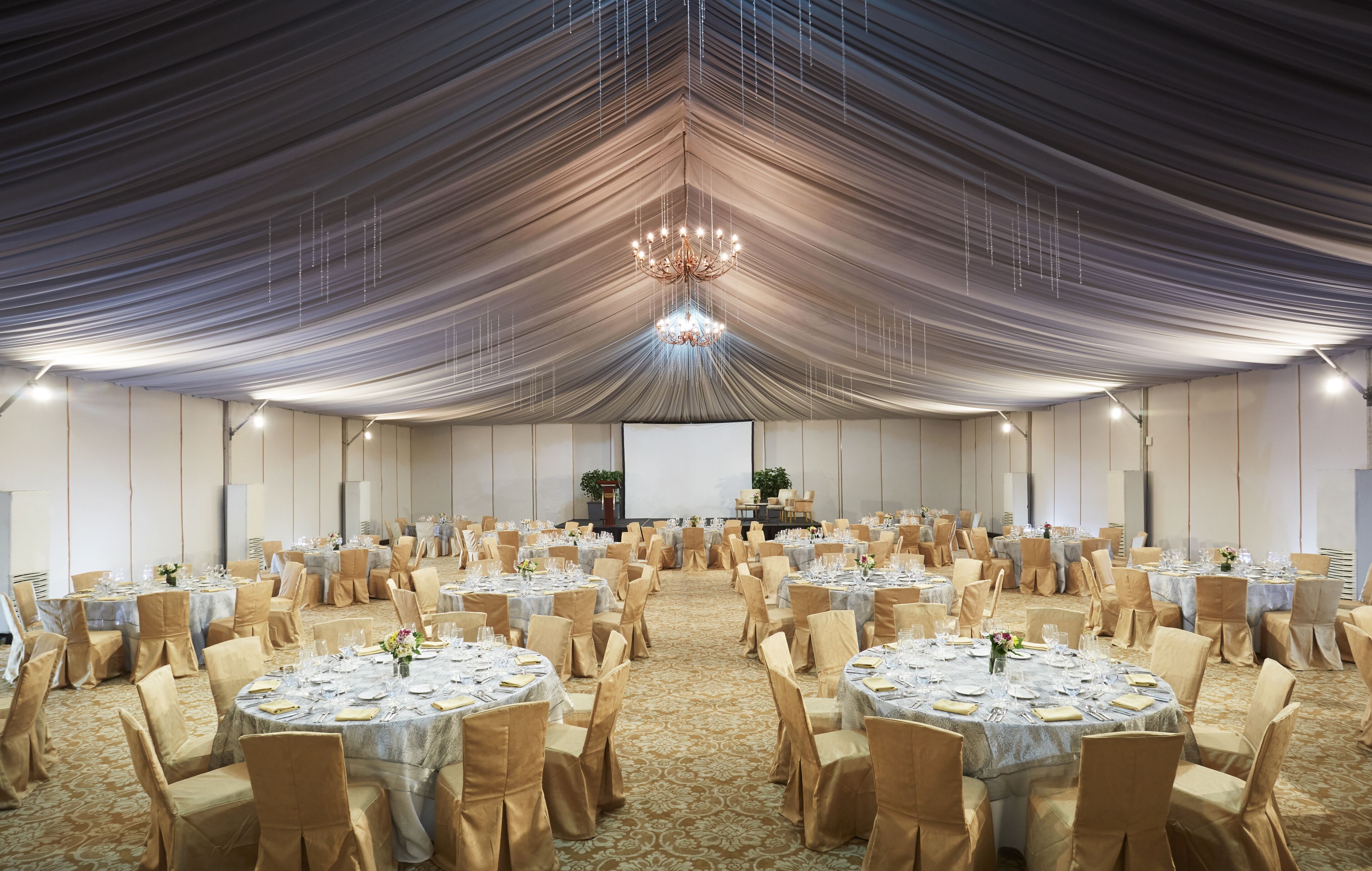 A large banquet hall with round tables, chairs, and a stage.
