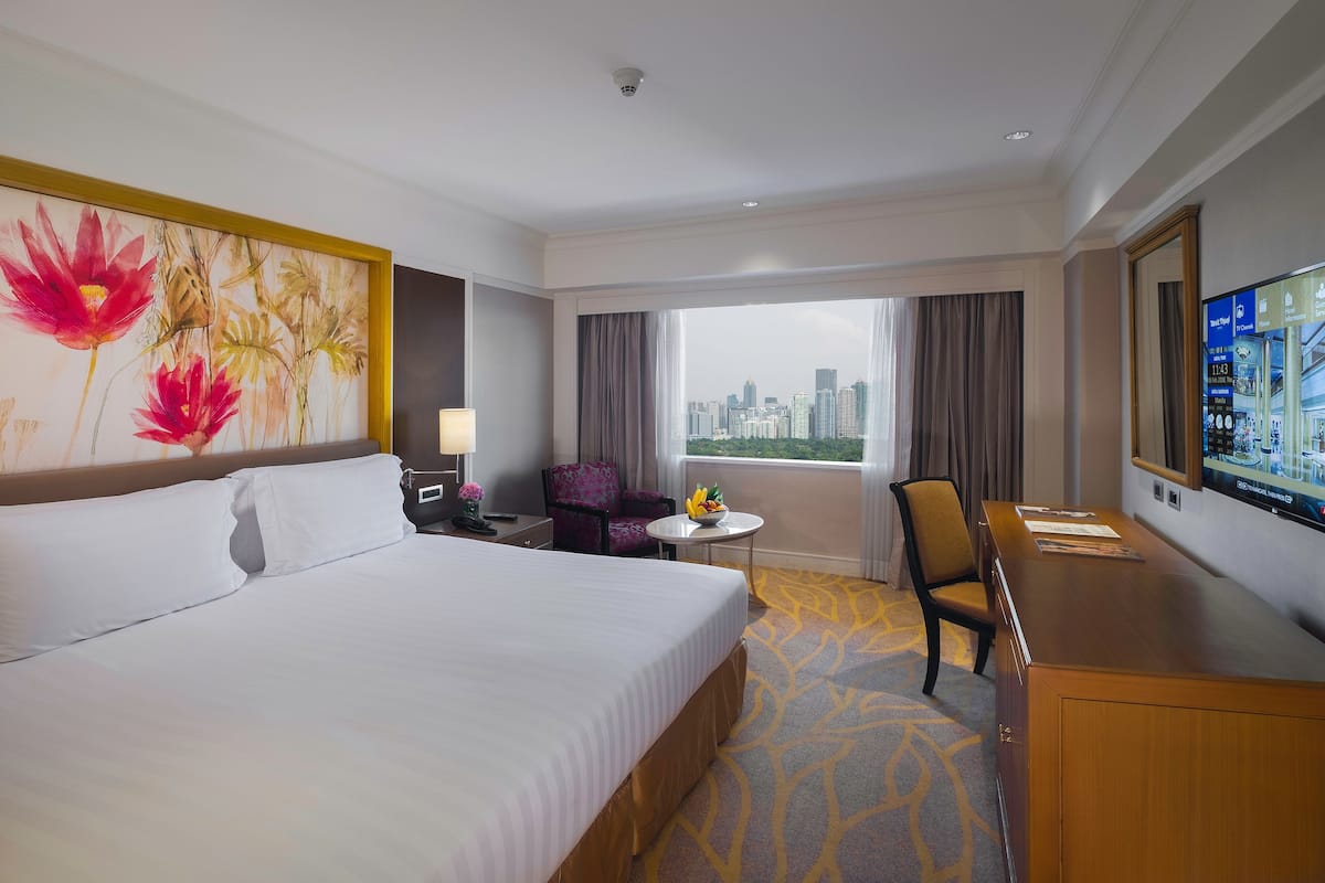 Habitación de hotel con una cama grande, un escritorio, una silla, una mesita con frutero y un televisor.