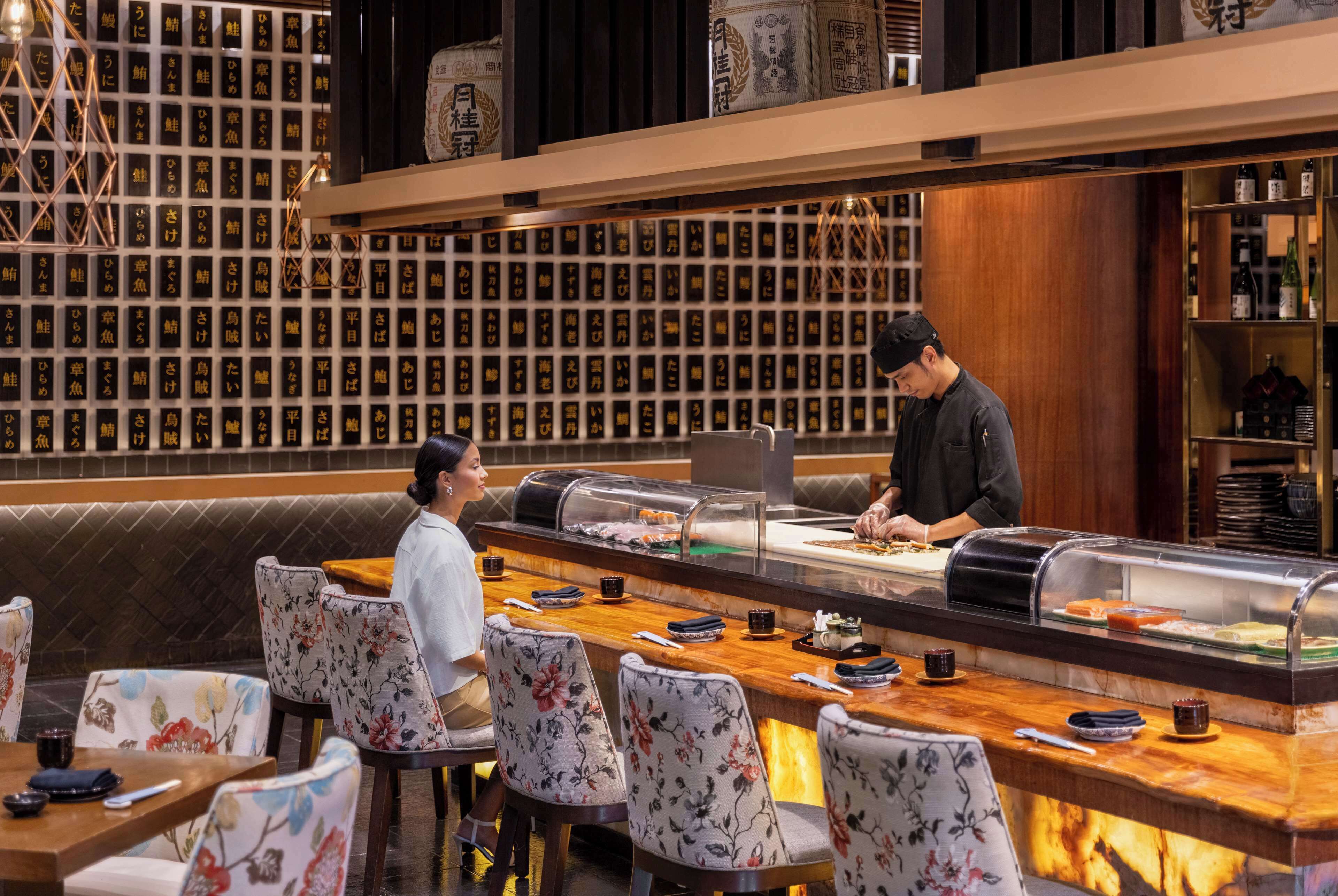 A restaurant with a sushi bar, wooden tables, and chairs.