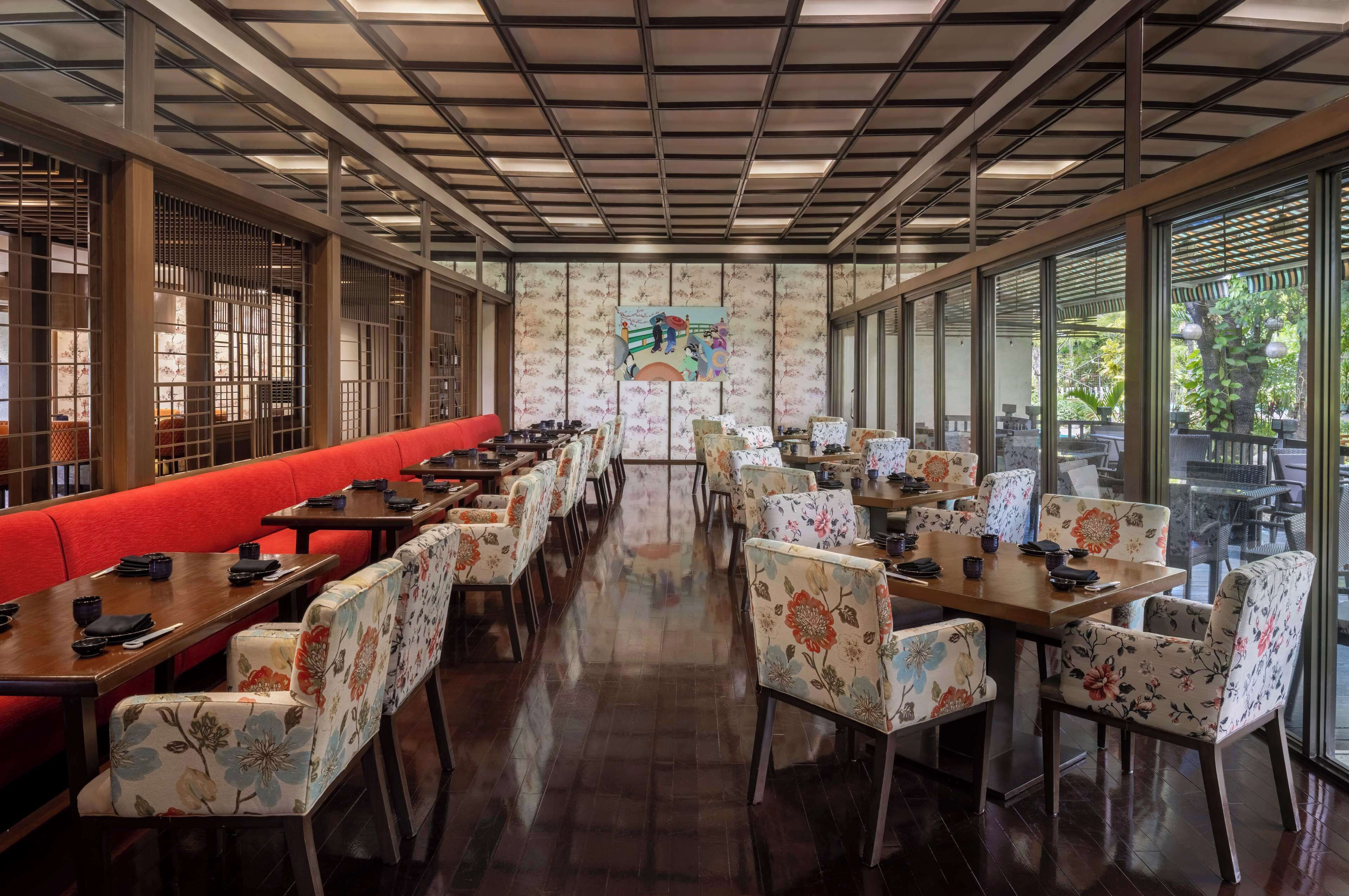 A restaurant with a long counter, red seating, and floral chairs.