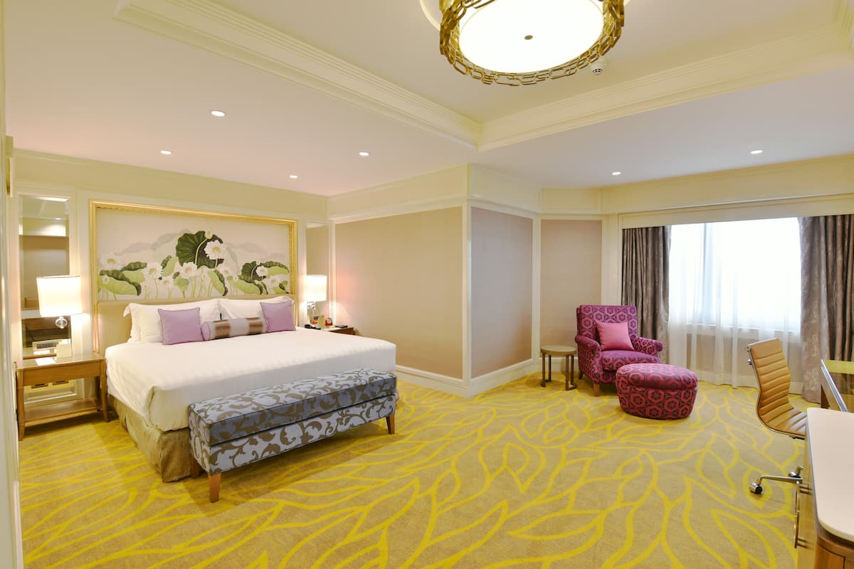 Una habitación de hotel con una cama grande, un banco, una silla y un escritorio.