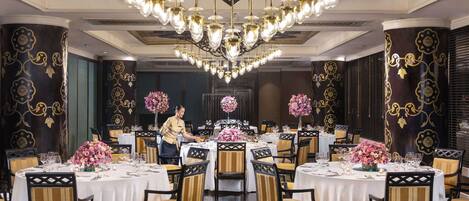 A formal dining room with round tables, chairs, and a chandelier.